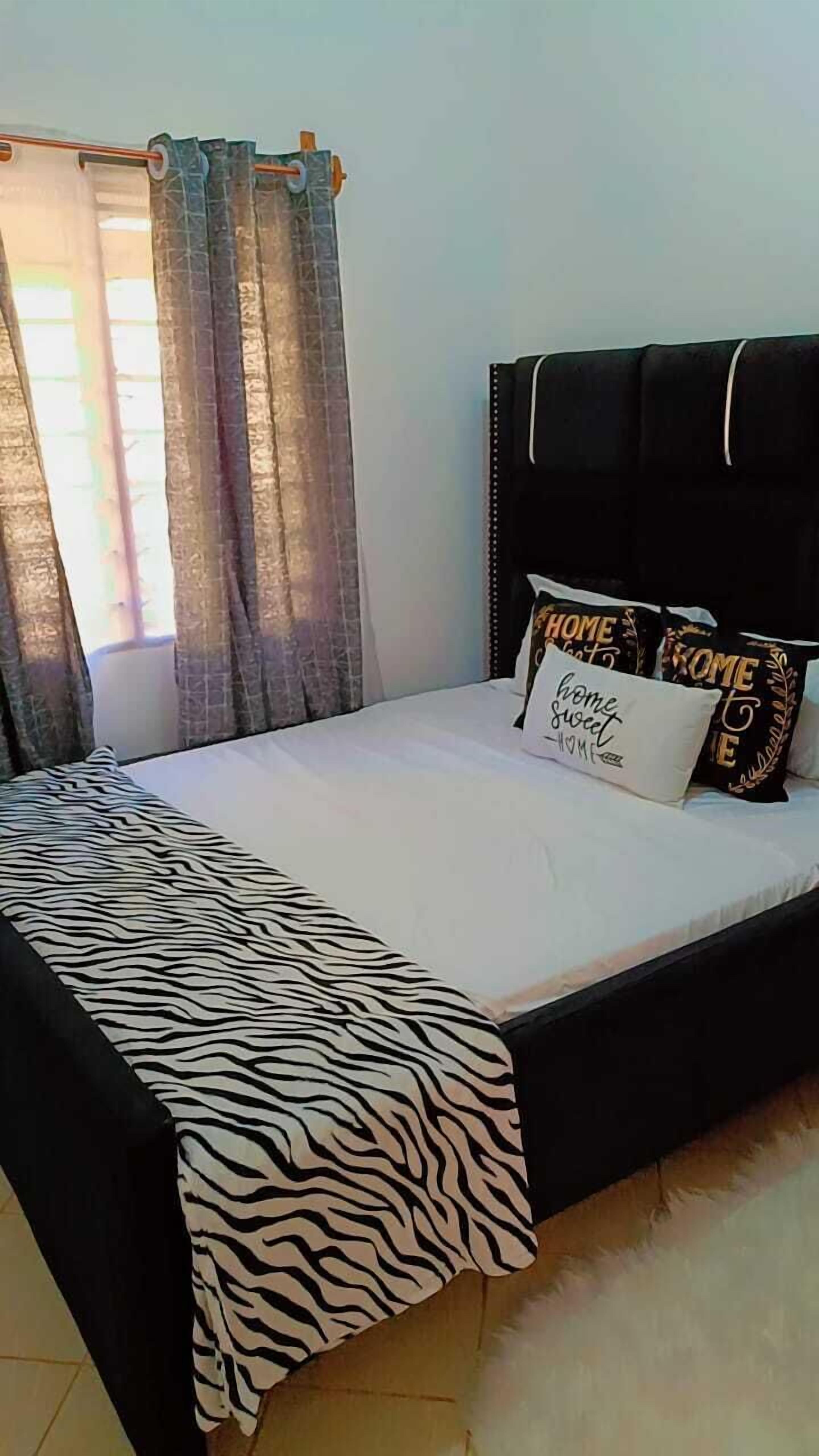 Una cama con colcha de estampado de cebra, cabecera negra y múltiples almohadas con la inscripción 'HOME SWEET HOME'.