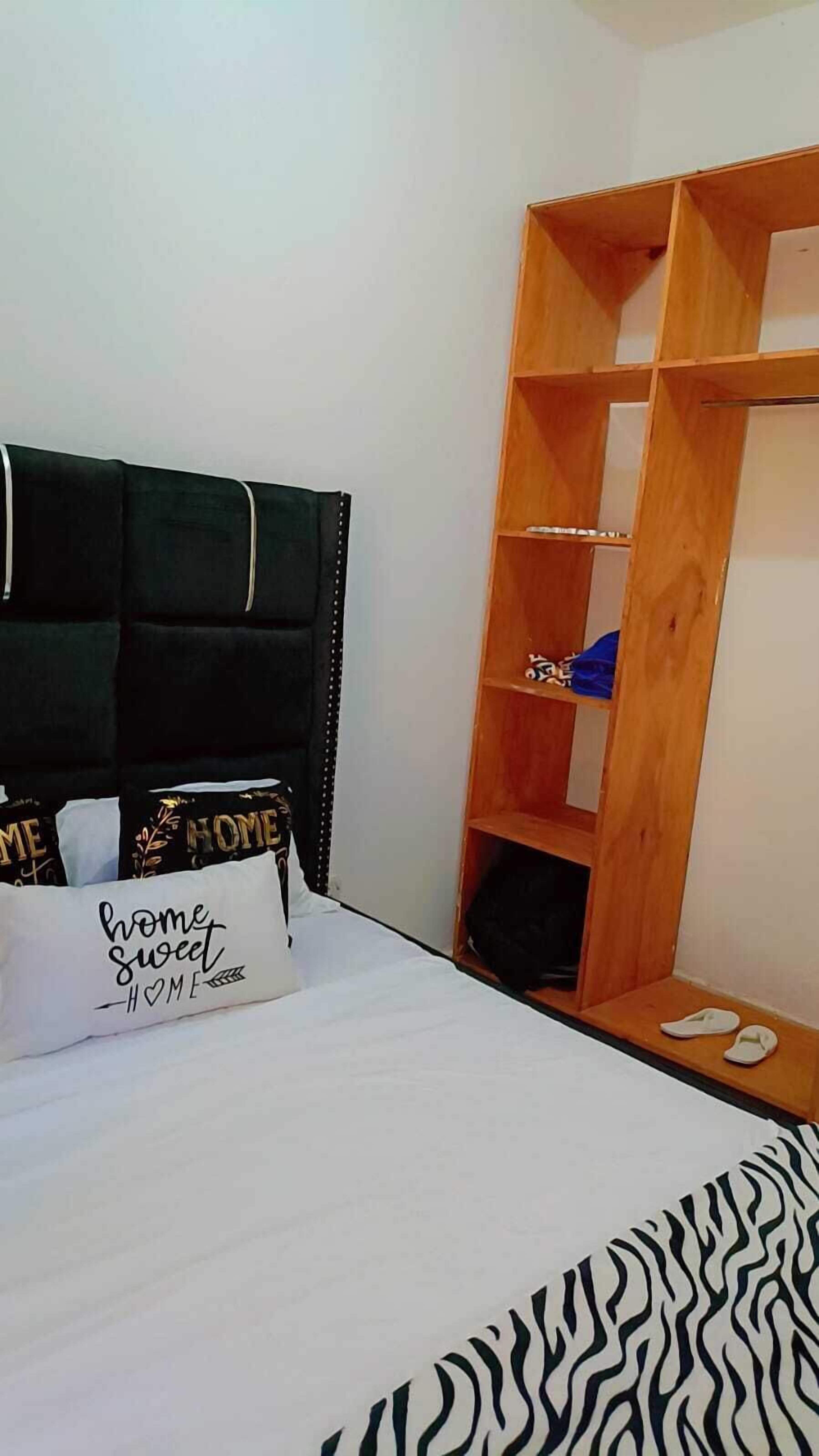 A bedroom with a bed, a wooden wardrobe, and a pillow with 'home sweet home' text.