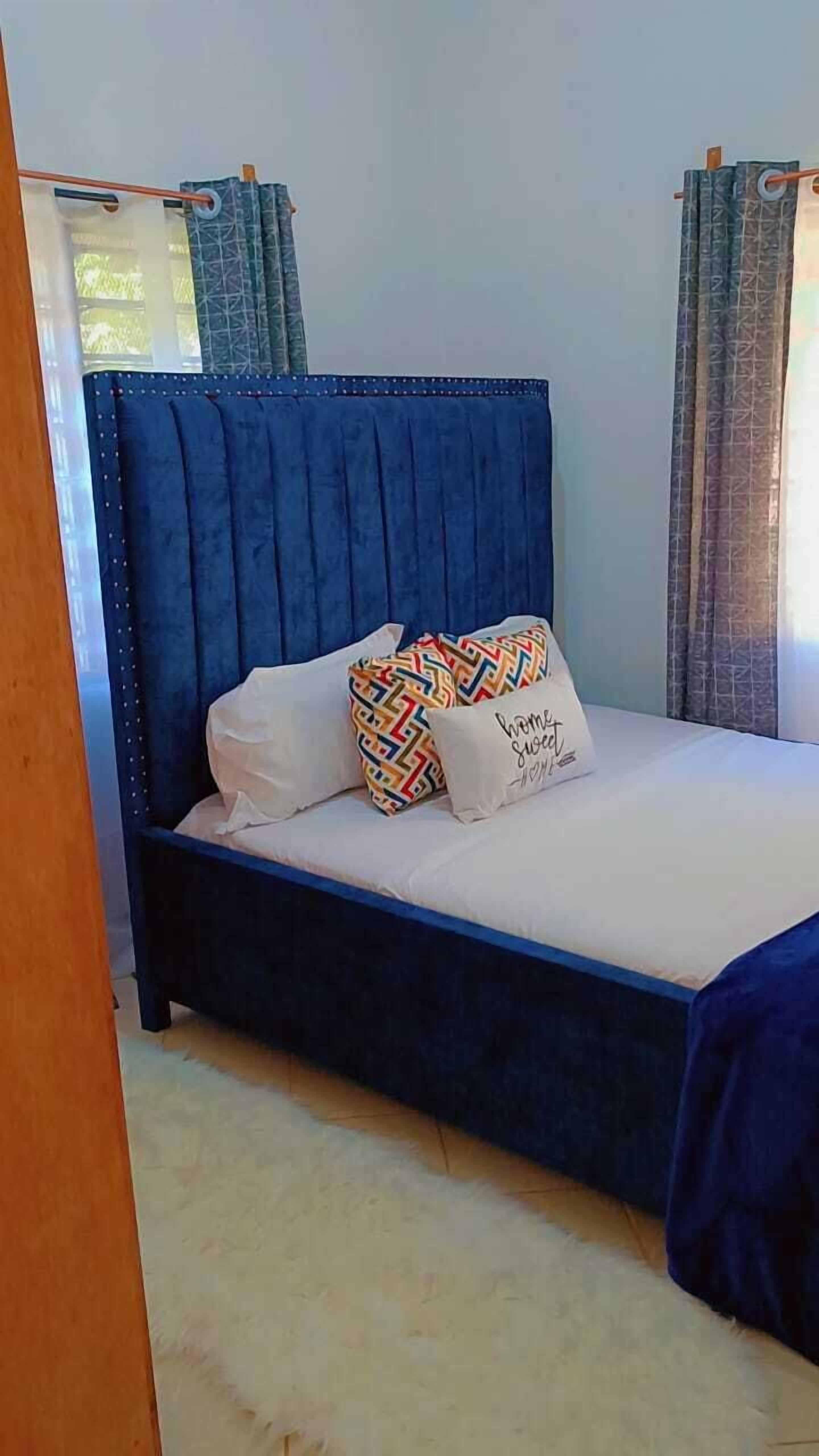 Una cama con cabecera azul, ropa de cama blanca y almohadas coloridas con estampados.