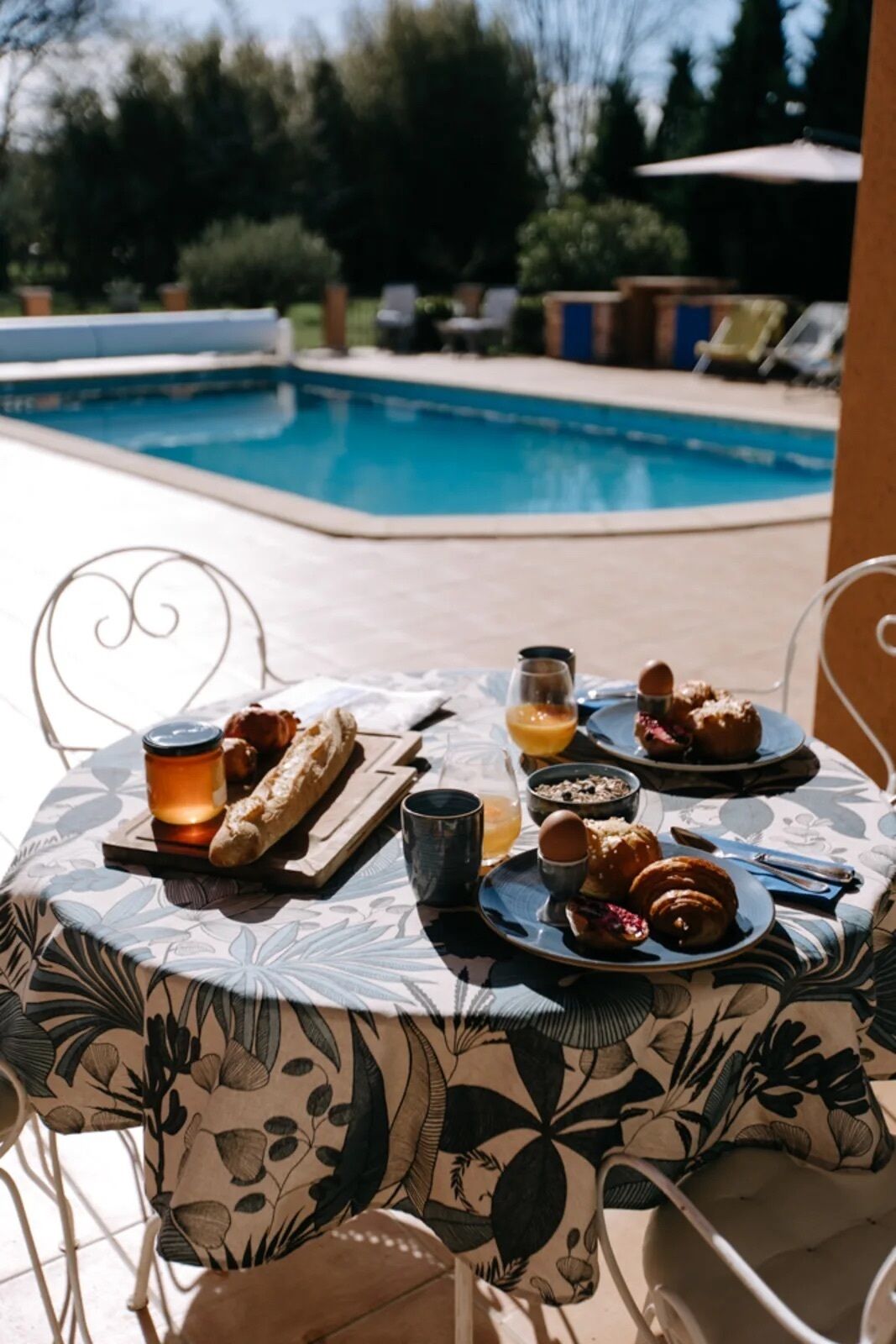 Mesa al aire libre con desayuno, una vela y vista a una piscina.