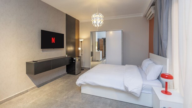 Una habitación de hotel moderna con una cama grande, un televisor montado en la pared, una mesita de noche y un espejo.