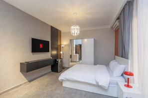 Et moderne hotelværelse med en stor seng, et fjernsyn ophængt på væggen, et sengebord og et spejl.