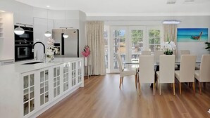 Une cuisine moderne dotée d’appareils électroménagers intégrés, un coin repas avec des chaises blanches et de grandes fenêtres.