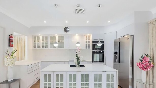 Une cuisine moderne avec des meubles blancs, un îlot central et un four encastré.