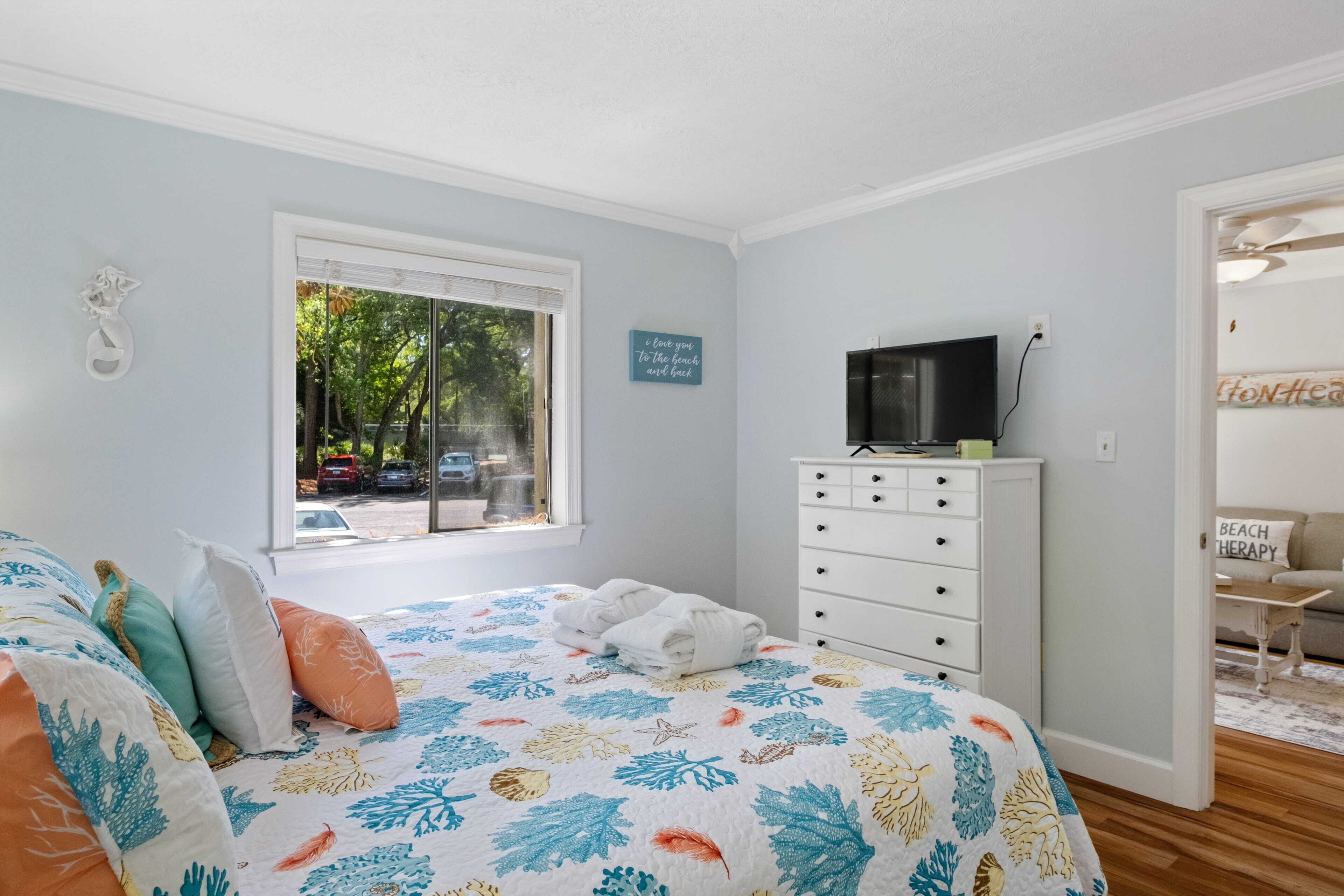 Quarto com cama, cômoda, televisão e janela com vista para a rua.