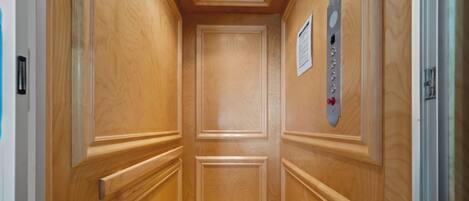 Um elevador estreito com painéis de madeira e piso de azulejos.
