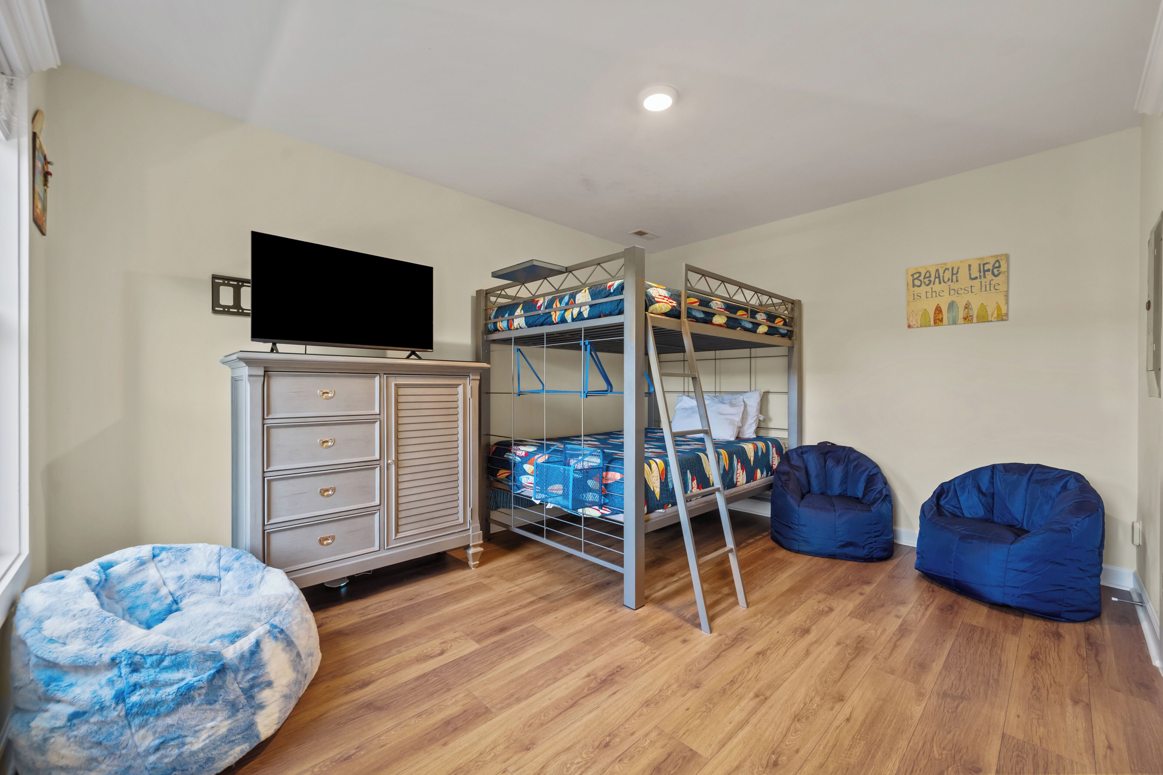 A room with a bunk bed, a dresser, a television, bean bags, and a wall sign.