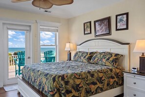 A bedroom with a bed, a nightstand, a lamp, and a view of the ocean through a door.