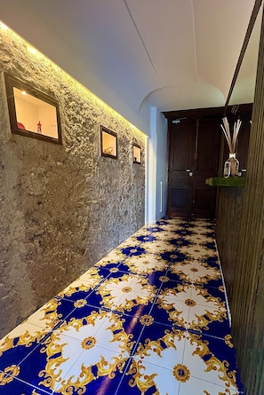 Un couloir avec un mur à texture, un sol à motifs et une porte en bois au fond.