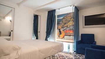 Una camera d'albergo con un letto, una poltrona blu, un quadro raffigurante una veduta costiera e un pavimento piastrellato.