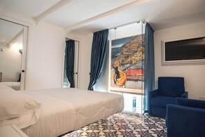 Une chambre d’hôtel avec un lit, un fauteuil bleu, un tableau représentant un paysage côtier et un sol carrelé.
