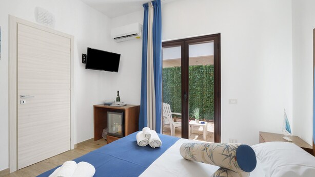 Una camera d'hotel con un letto, una televisione, una scrivania con un computer, una sedia e vista su un giardino verde attraverso la finestra.