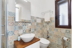 A bathroom with a white sink, a mirror, a toilet, and a patterned tile backsplash. - Room 'La Rocca 2' with Private Terrace, Wi-Fi and Air Conditioning (San Vito Lo Capo)
