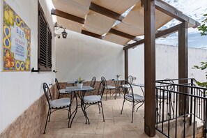 An outdoor patio with tables and chairs, a pergola, and a wall with a sign. - Room 'La Rocca 2' with Private Terrace, Wi-Fi and Air Conditioning (San Vito Lo Capo)