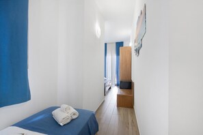 A narrow hotel room with a bed, a wooden bench, and a wall-mounted TV.