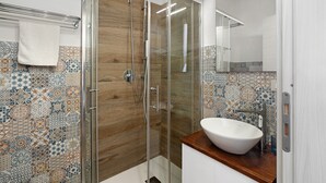 Une salle de bain moderne avec une douche à parois de verre, un meuble-lavabo en bois, un lavabo blanc et des murs recouverts de carreaux à motifs.