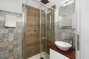 A modern bathroom with a glass-enclosed shower, a wooden vanity, a white sink, and patterned tile walls.