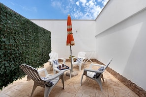A patio with white chairs, a table, and an umbrella.