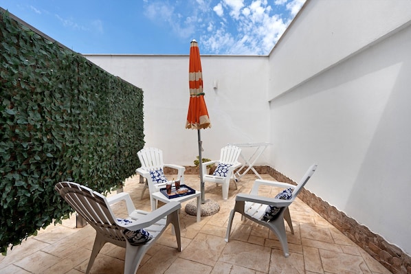 A patio with white chairs, a table, and an umbrella.