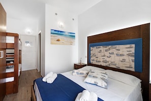 A bedroom with a bed, a wooden wardrobe, a nightstand, a wall-mounted painting, and a door.