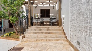 Un espace extérieur abrité, aménagé avec des sièges, et accessible par un escalier menant à l’entrée d’un bâtiment.