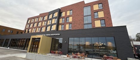 A modern hotel with a flat roof, large windows, and outdoor seating.