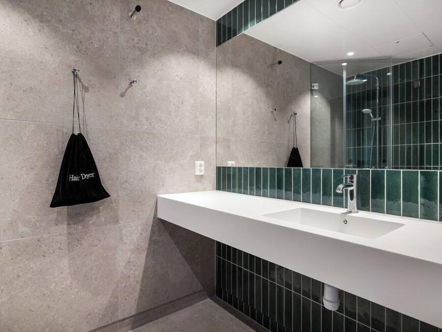Un baño moderno con un lavamanos blanco, un espejo grande y una zona de ducha.