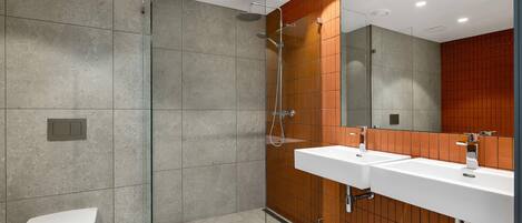 A modern bathroom with a glass-enclosed shower, a white toilet, and a double sink with a wooden panel backsplash.