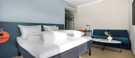 Una habitación de hotel moderna con cama, sofá, una mesita y un calentador en la pared.