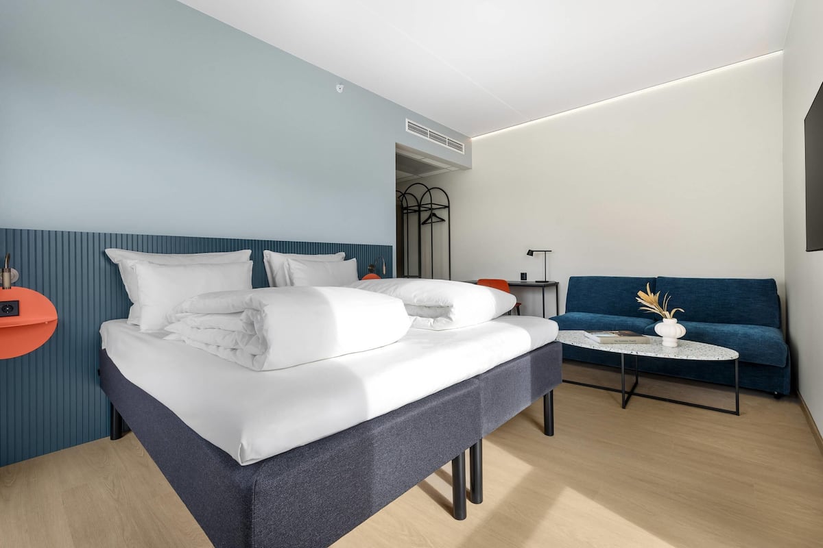 Ein modernes Hotelzimmer mit einem Bett, einer Couch, einem kleinen Tisch und einem Wandhaken für Kleidung.