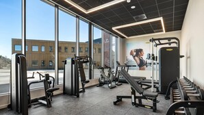 A gym with exercise equipment, large windows, and a view of a building outside.