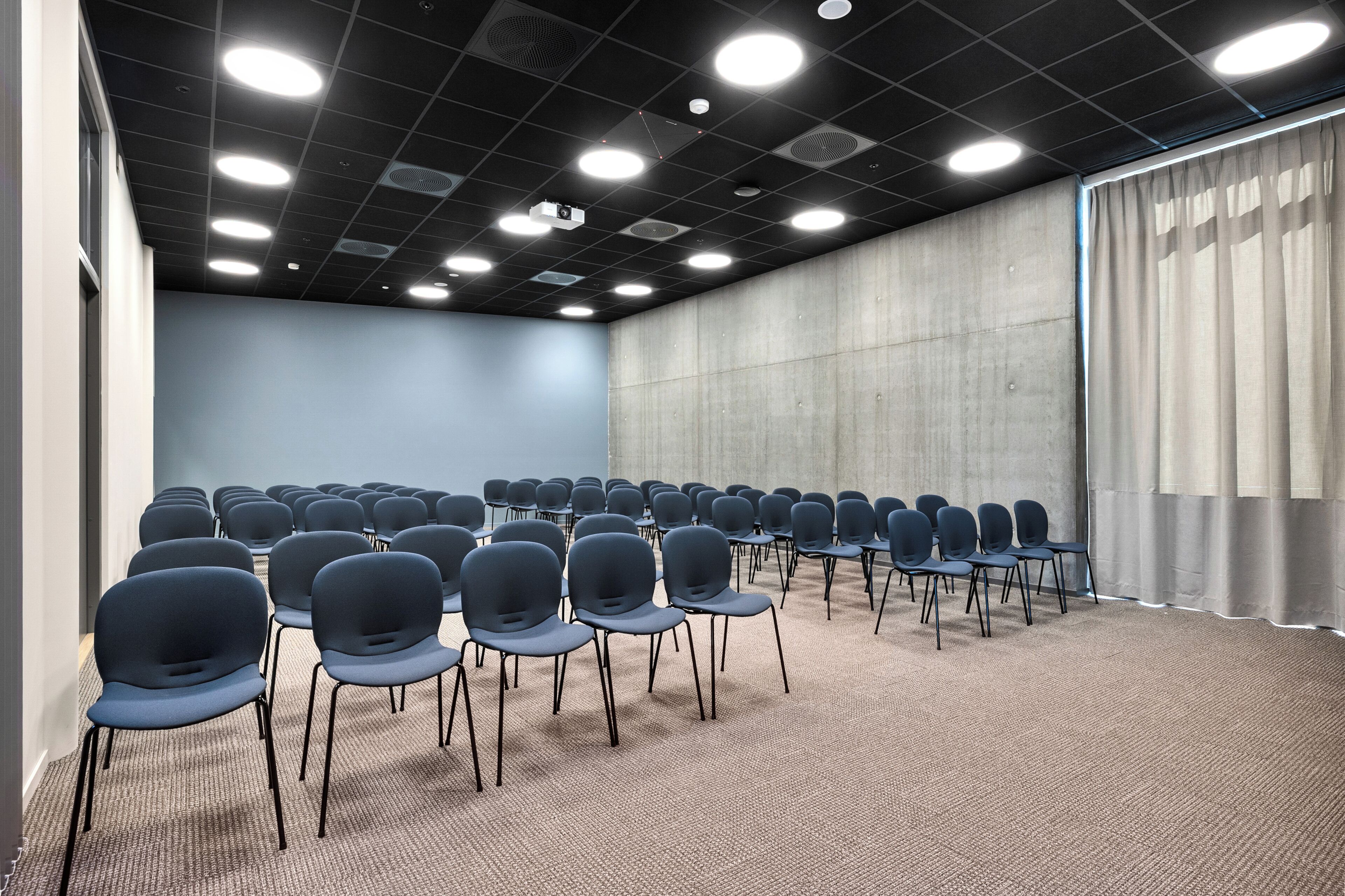 A conference room with rows of chairs, a carpeted floor, and a ceiling with recessed lighting.