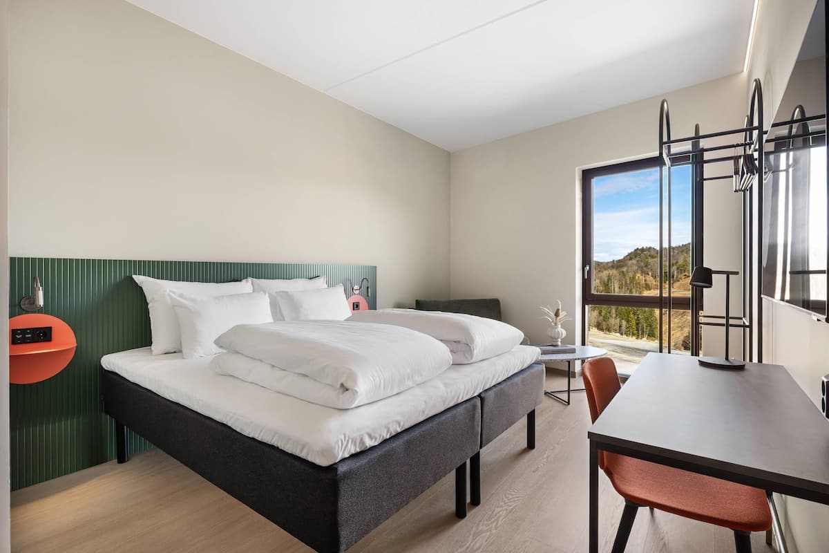 Ein modernes Hotelzimmer mit Bett, Schreibtisch und Blick ins Freie.