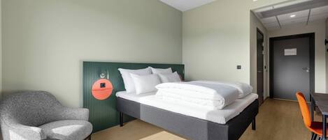 A hotel room with a bed, a chair, a table, and a door.