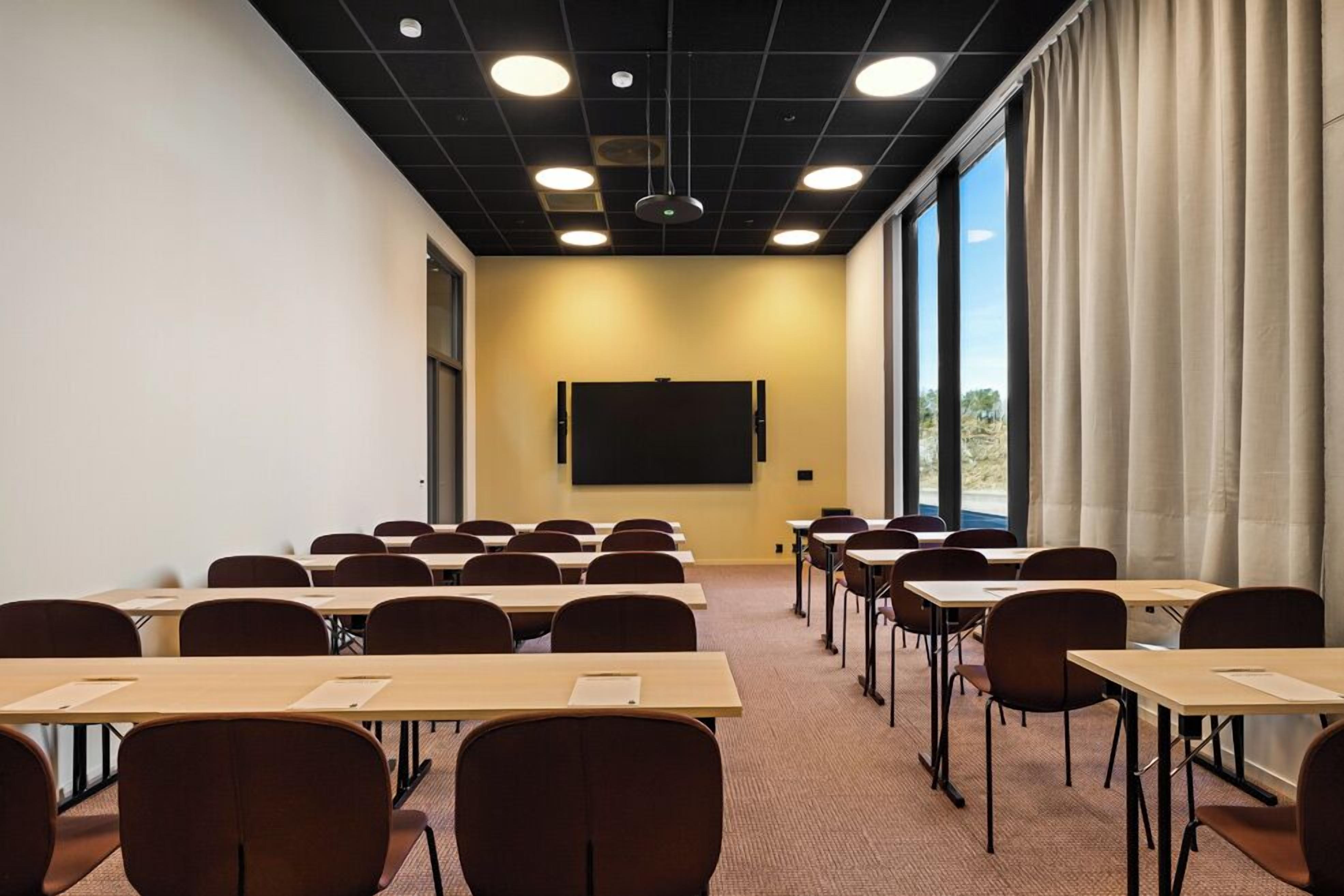 A conference room with tables and chairs, a projector screen, and large windows with curtains.