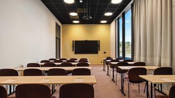 A conference room with tables and chairs, a projector screen, and large windows with curtains.