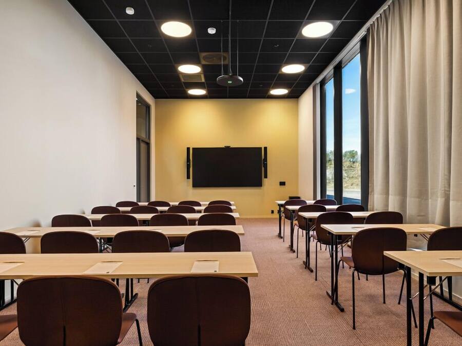 A conference room with tables and chairs, a projector screen, and large windows with curtains.
