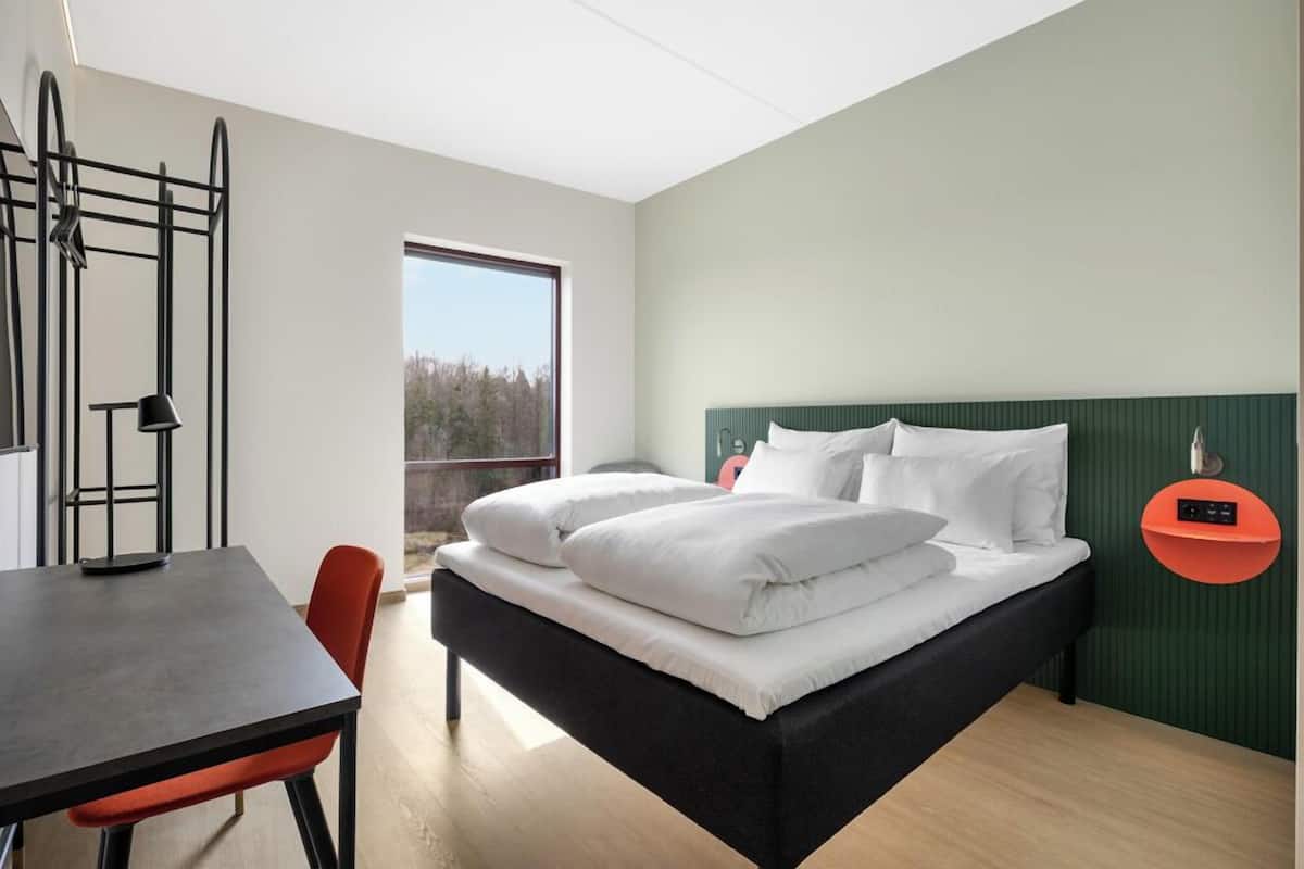 Ein modernes Hotelzimmer mit Bett, Schreibtisch und Stuhl.