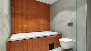 Moderni kylpyhuone, jossa on suuri kylpyamme, wc ja lasinen suihkuseinä.