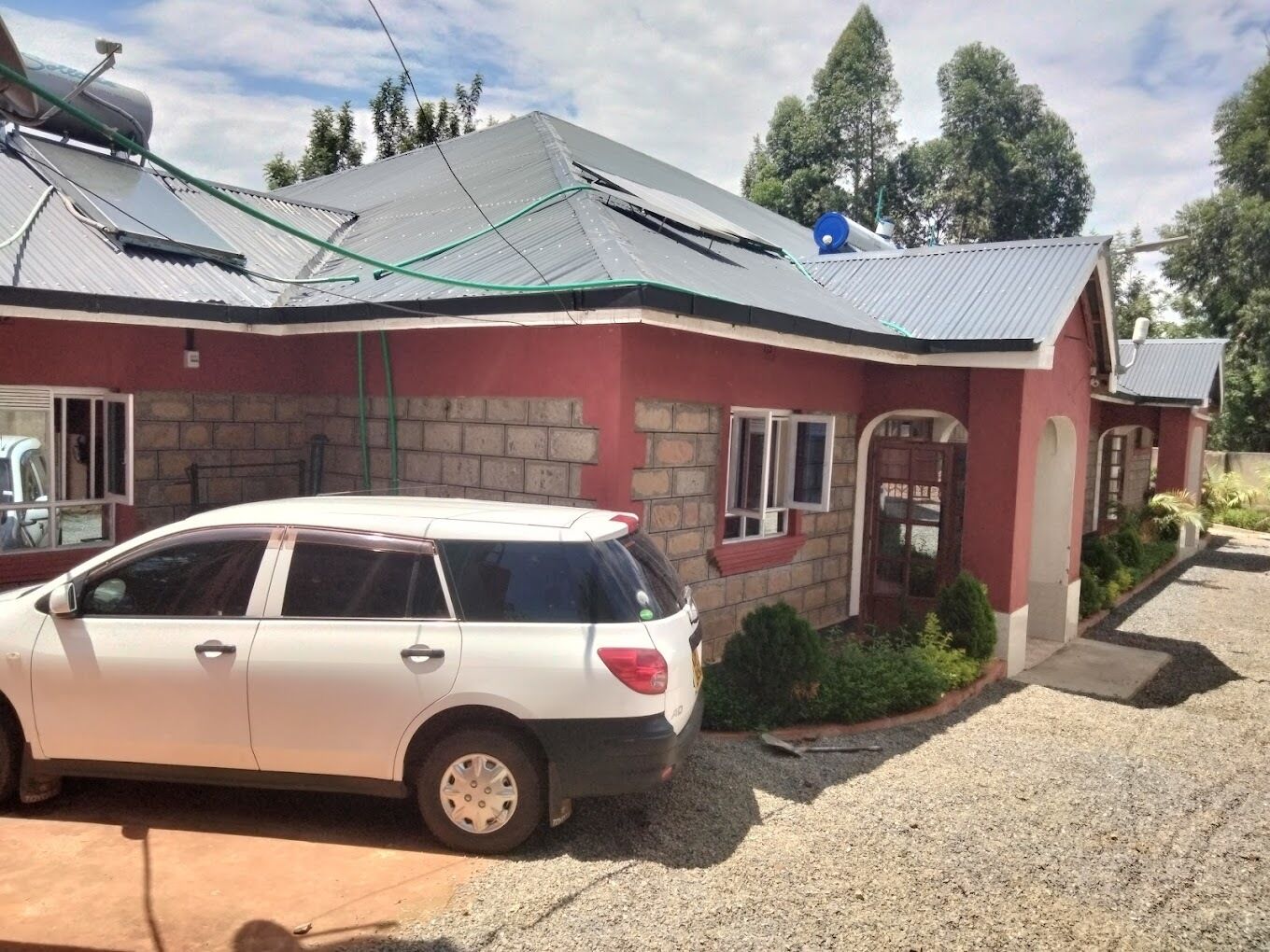 A house with a car parked in front, a sloped roof, and a stone wall.