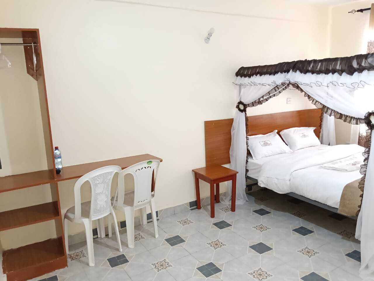A bedroom with a bed, a desk, two chairs, and a bedside table.