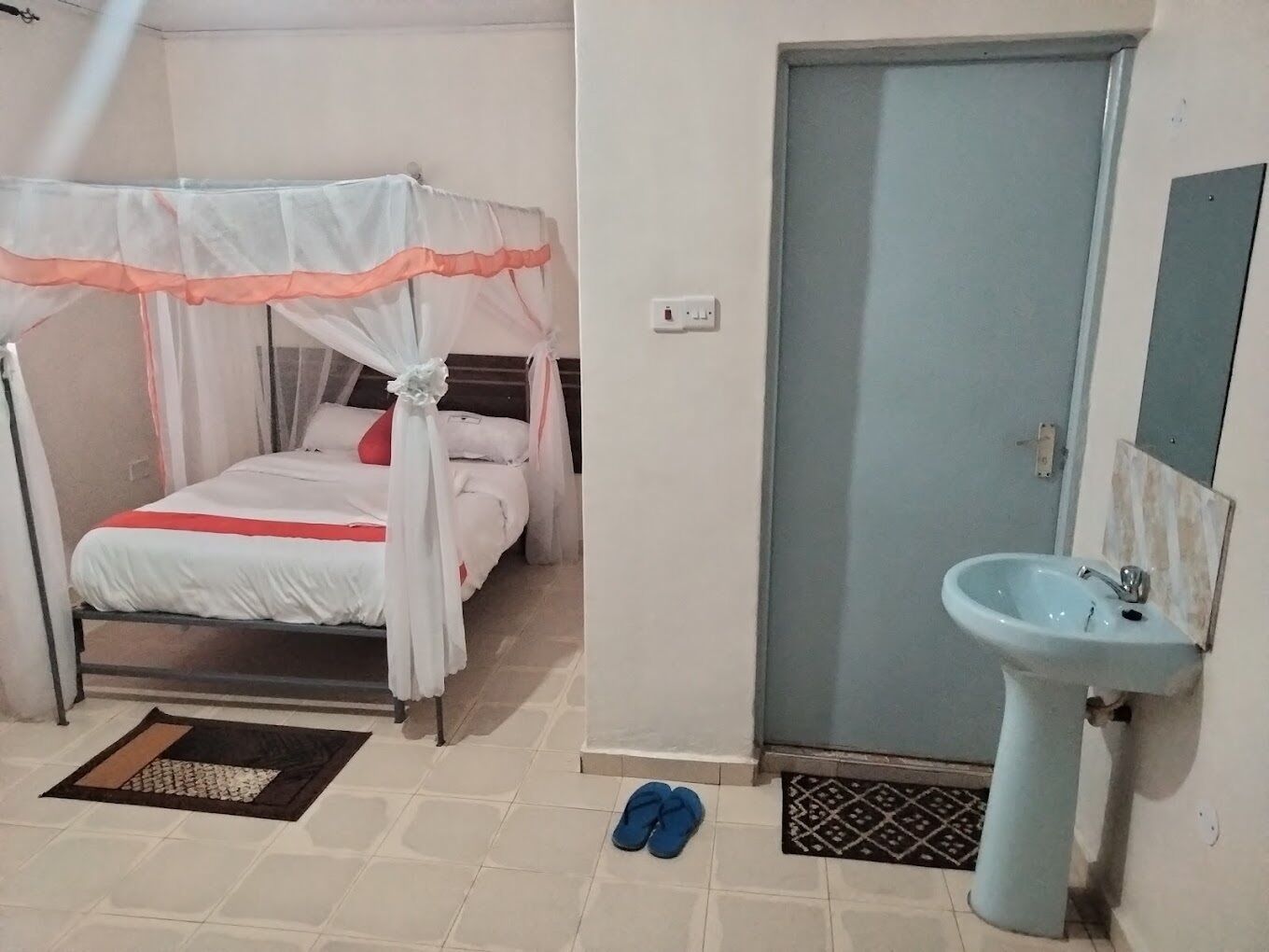 A bedroom with a bed, a canopy, a sink, and a door.