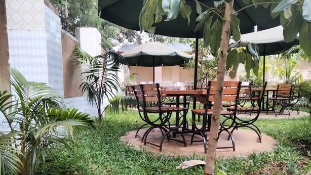 An outdoor seating area with round tables and chairs, surrounded by greenery and a tiled wall. - Good Morning Hotel Rongo (Rongo)