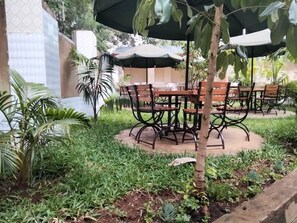An outdoor seating area with round tables and chairs, surrounded by greenery and a tiled wall. - Good Morning Hotel Rongo (Rongo)