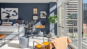 Une chambre moderne équipée d’un lit, d’un bureau, d’une chaise et de grandes fenêtres donnant sur la ville.