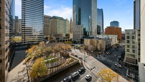 Une vue urbaine avec des immeubles modernes de grande hauteur, une place centrale bordée d’arbres et un ciel dégagé.