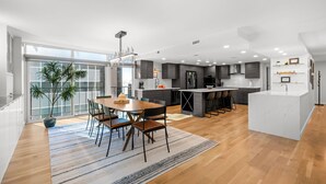 Une cuisine moderne dotée d’un îlot central, d’un coin repas avec une table et des chaises en bois, et d’une grande fenêtre offrant une vue dégagée.