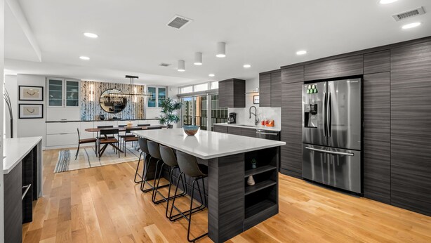 Une cuisine moderne dotée d’un îlot central, de meubles de couleur sombre et d’appareils électroménagers en acier inoxydable.