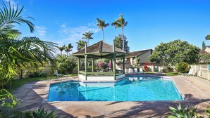 Una piscina con un pabellón, palmeras y una casa al fondo.