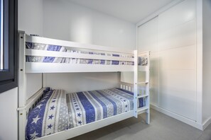 Un lit superposé avec une couvre-lit à motifs, une armoire blanche et une fenêtre.